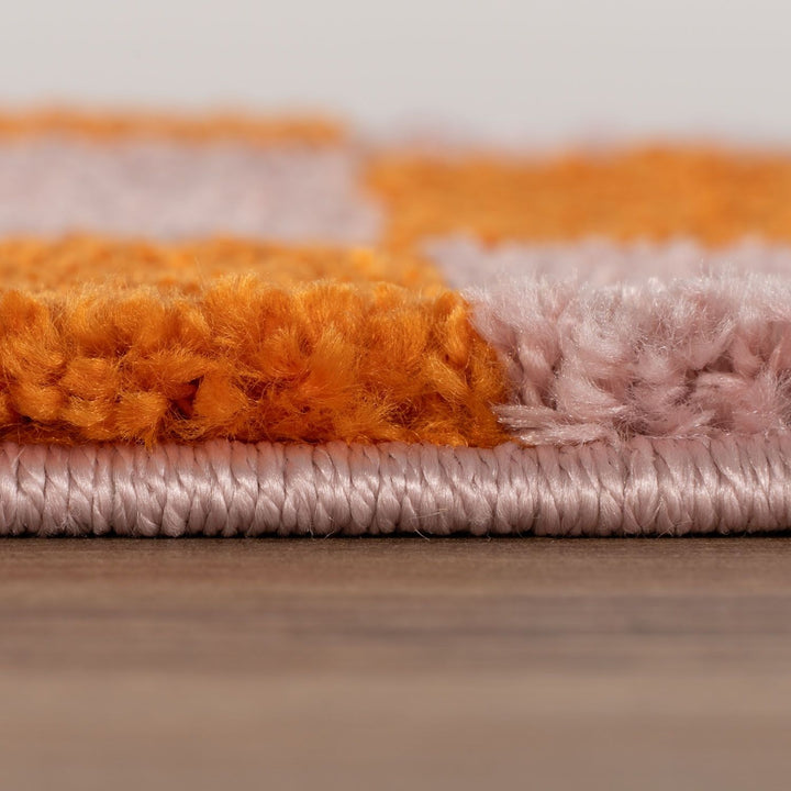 Close-up of a textured rug with orange, pink, and gray colors on a wooden floor.