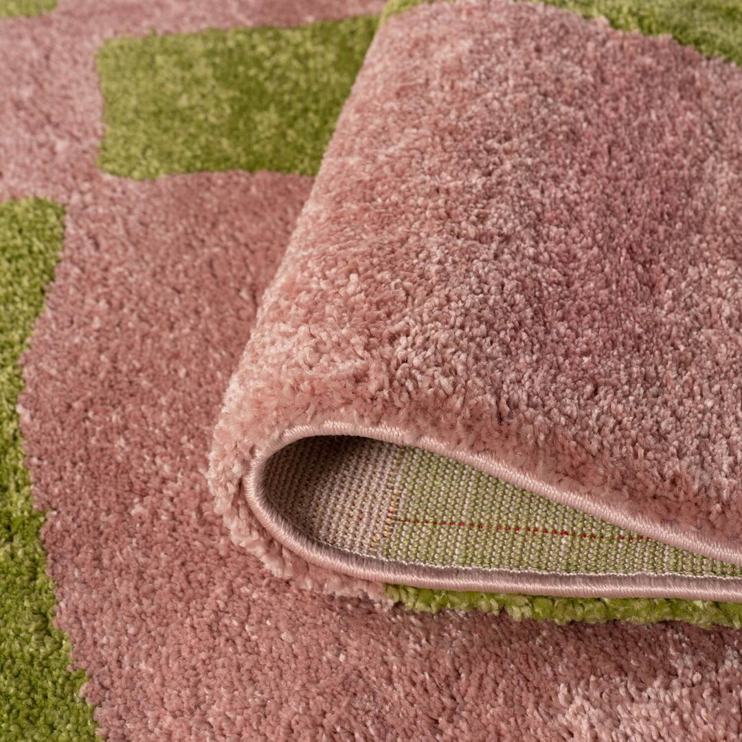 Close-up of a pinkish-brown textured rug with a green checkered pattern underneath.