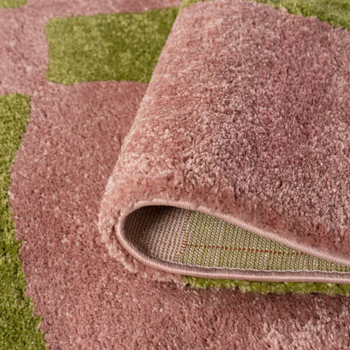 Close-up of a pinkish-brown textured rug with a green checkered pattern underneath.