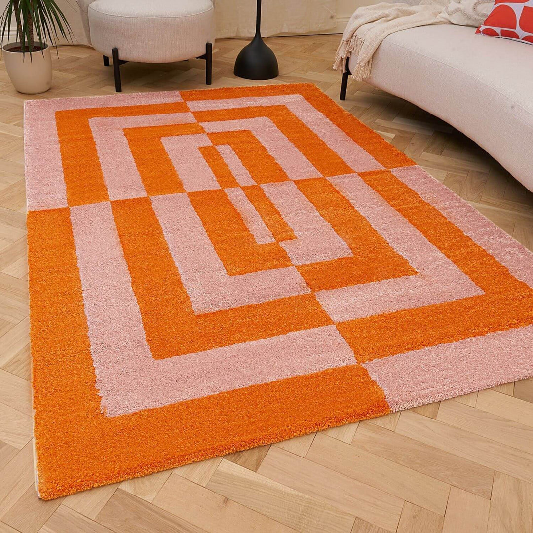 Geometric patterned orange and pink rug on a wooden floor