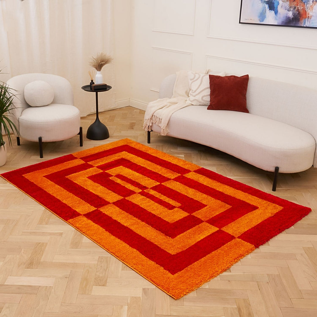 Red and orange geometric rug on a wooden floor with a white sofa and chair in the background.