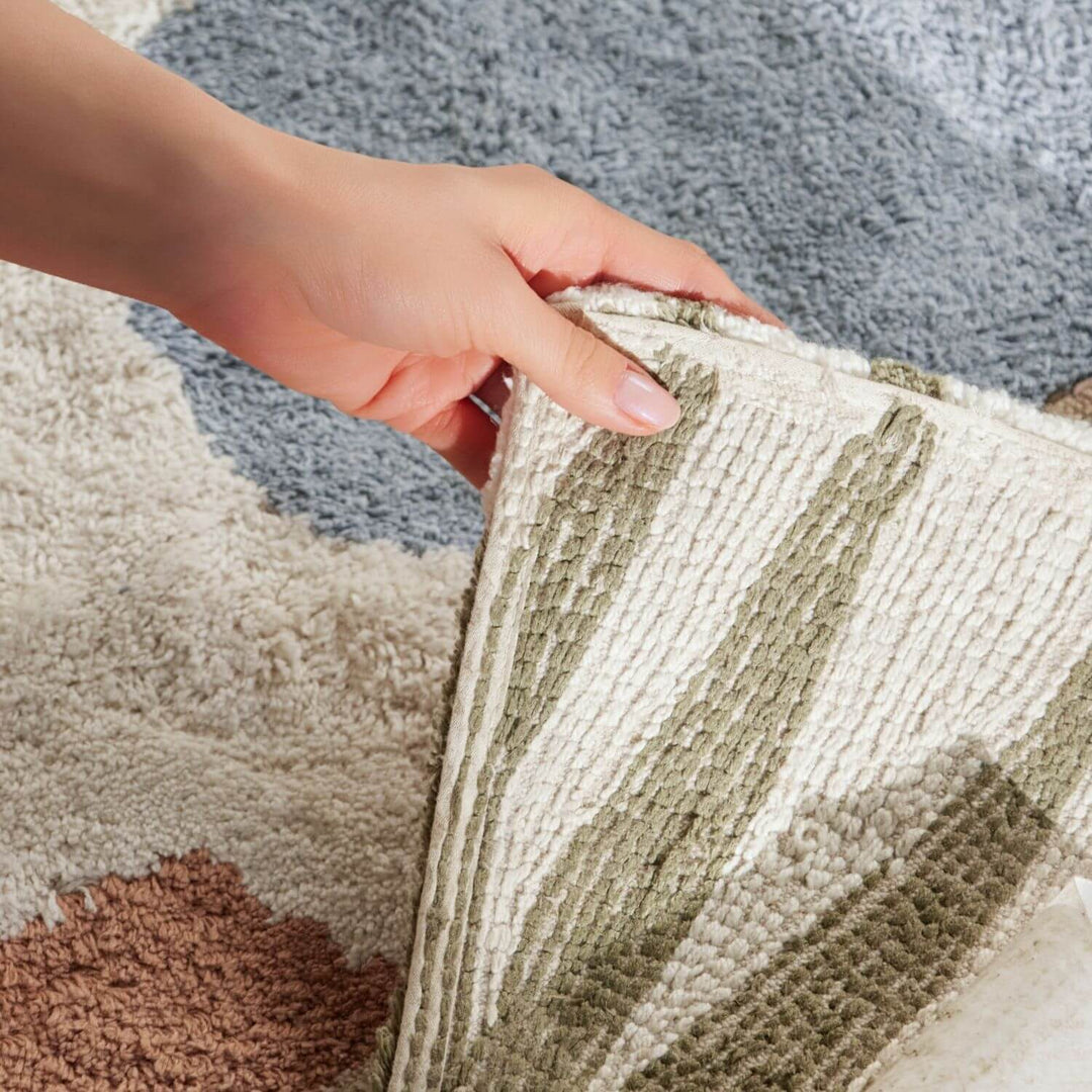 Close-up of a hand touching a textured rug with a neutral color palette.