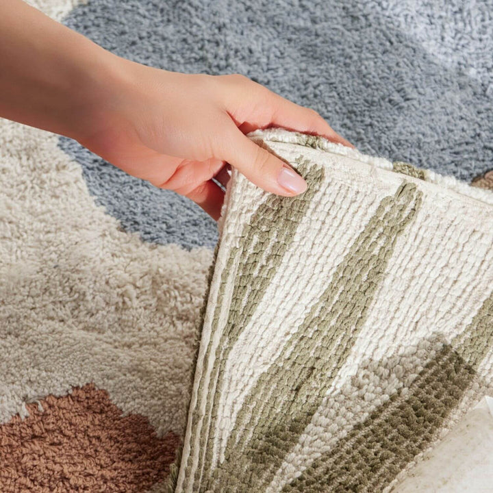 Close-up of a hand touching a textured rug with a neutral color palette.