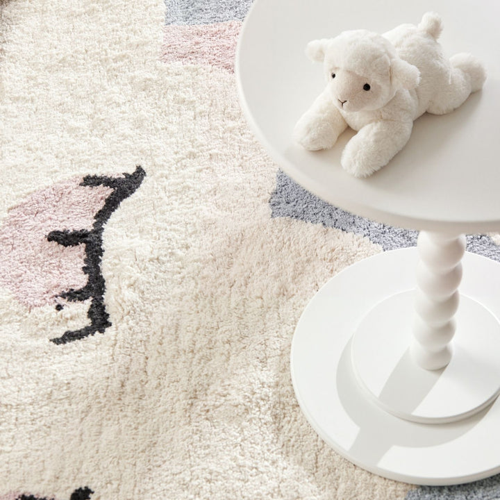 White teddy bear on a white stool next to a textured rug with abstract patterns