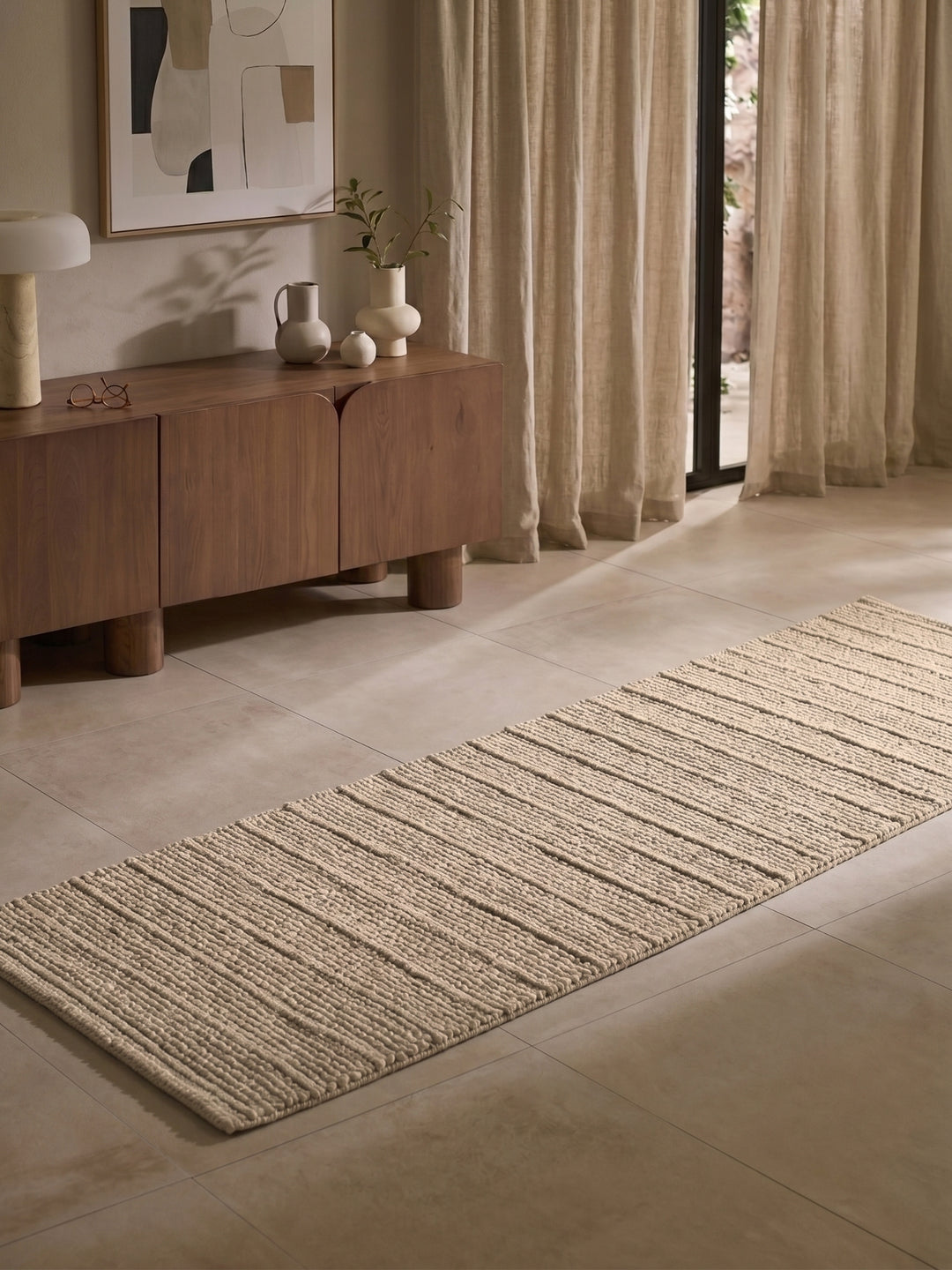 Beige rug on a tiled floor with a wooden sideboard and abstract art in the background.