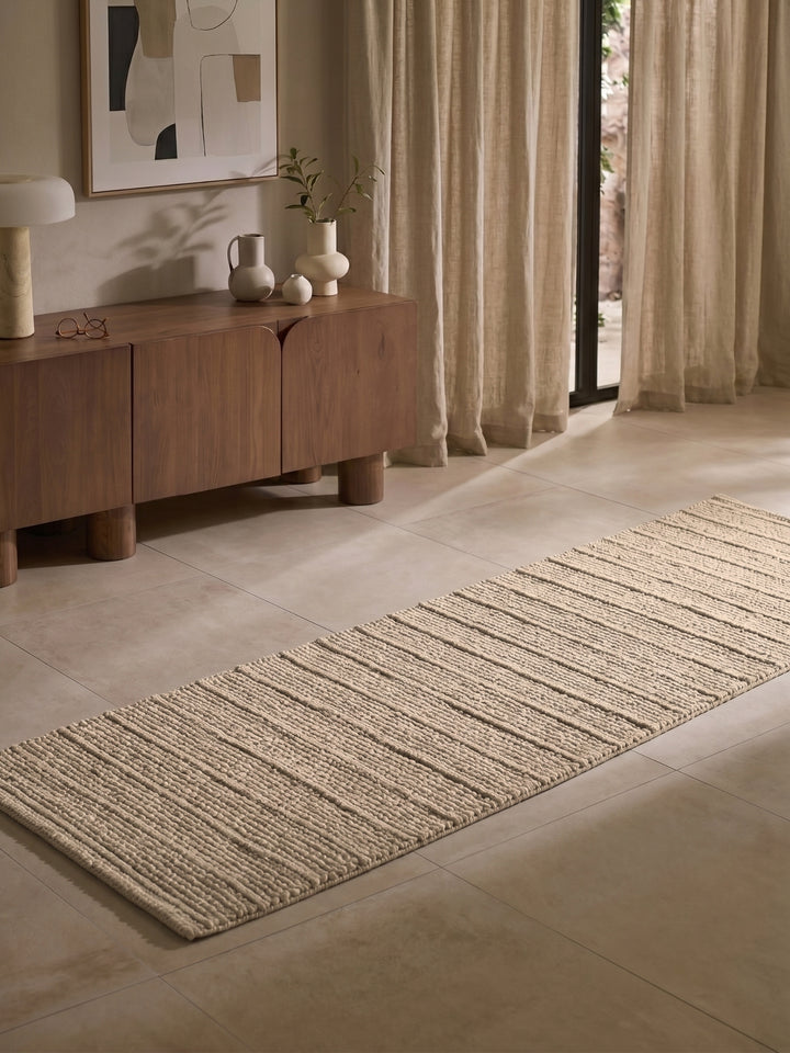 Beige rug on a tiled floor with a wooden sideboard and abstract art in the background.