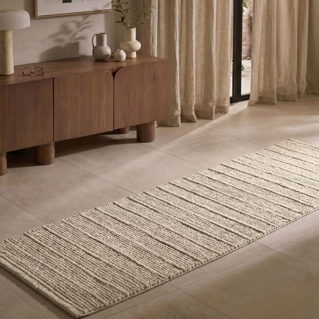 Long rectangular rug on a tiled floor in a room with wooden furniture and curtains.