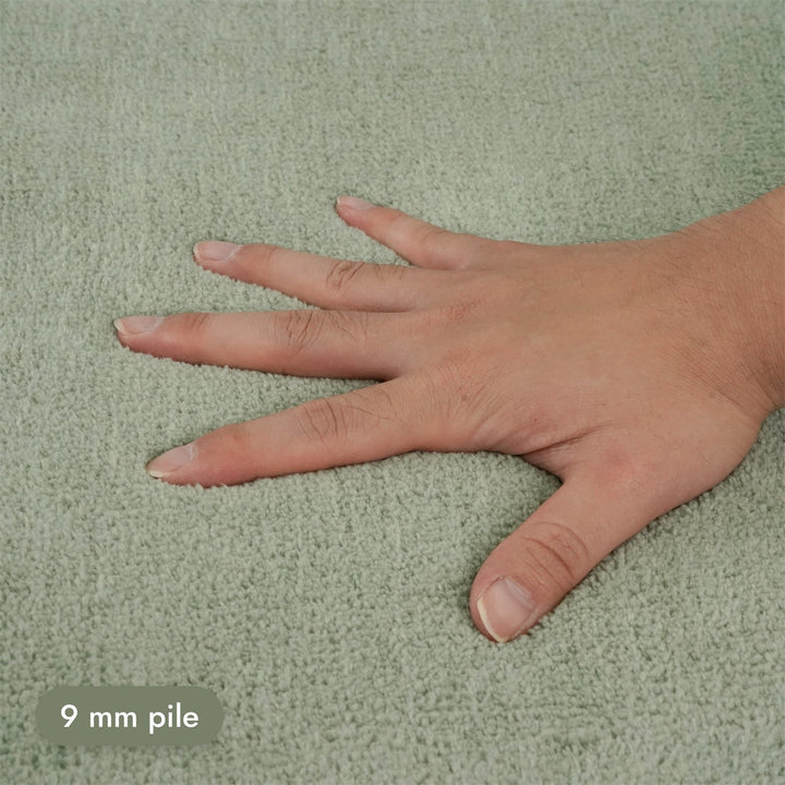 Washmellow sage green washable rug, close-up of the soft 9mm pile under a hand | The Rugs
