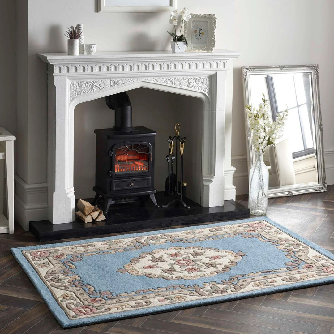 White fireplace with a black stove, decorative items, and a patterned rug on a wooden floor.