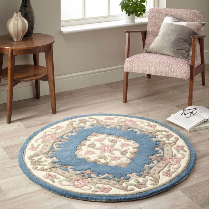 Round decorative rug with floral pattern on a wooden floor, surrounded by a chair and small table.