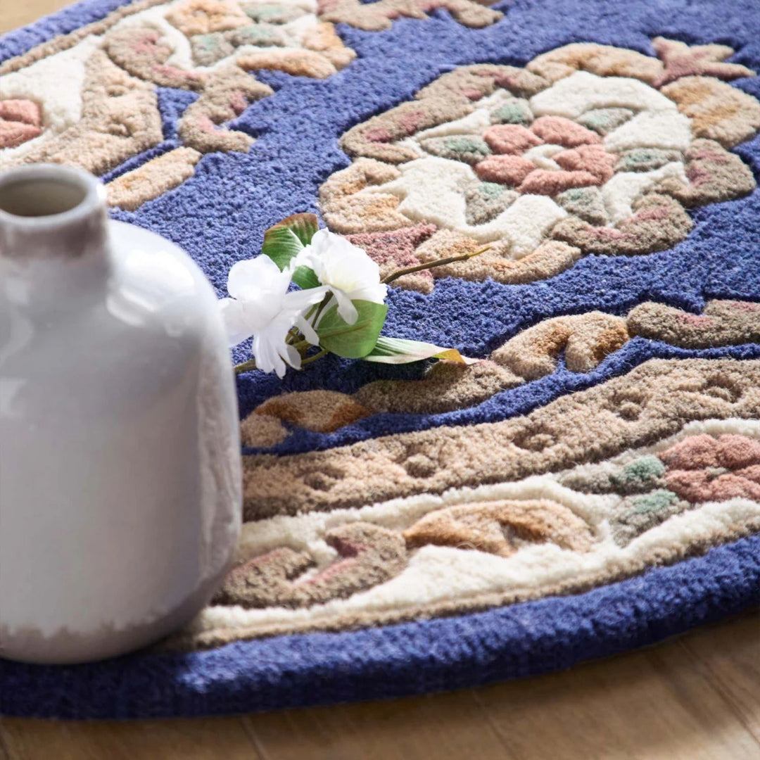 Decorative rug with floral pattern on a wooden floor, featuring a vase and flowers.