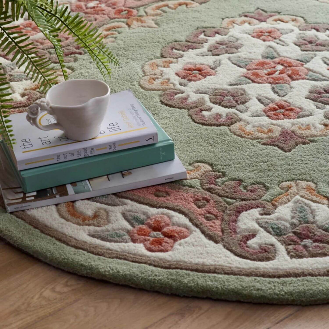 Decorative round rug with floral patterns on a wooden floor, featuring a cup and books.