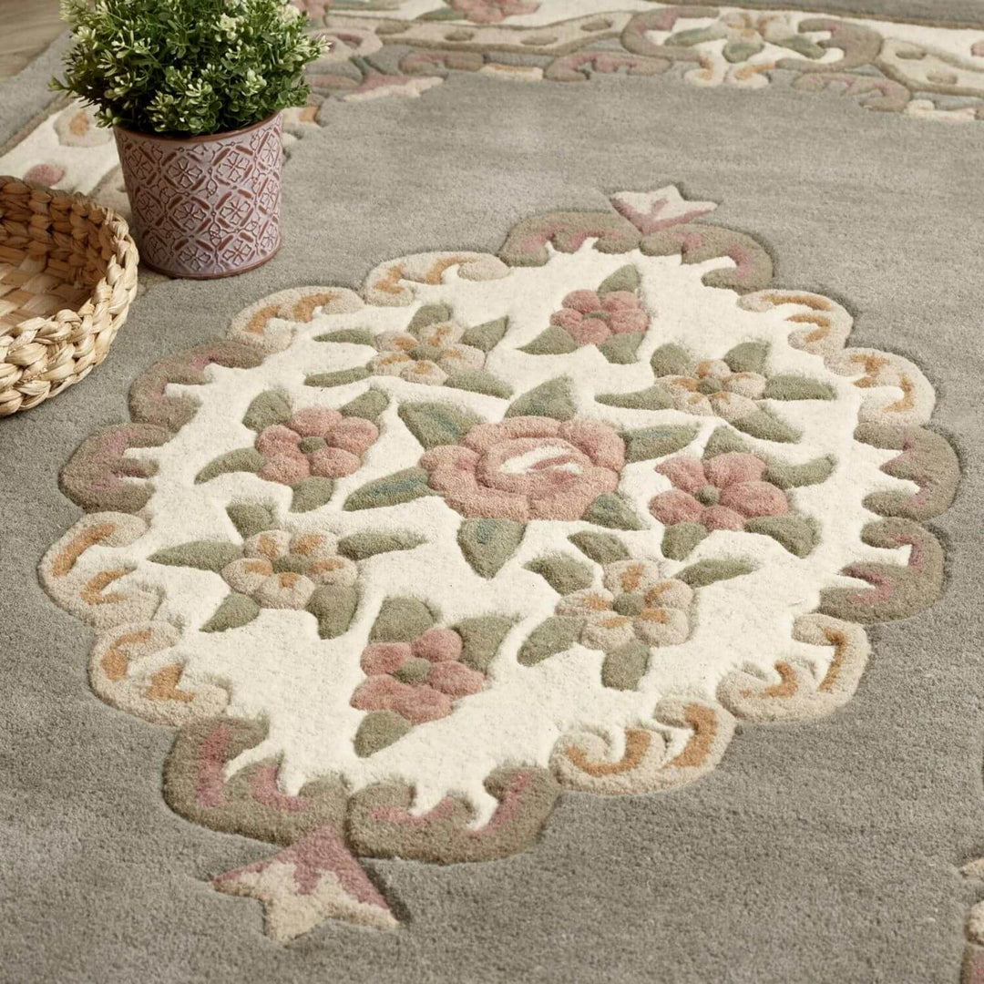 Decorative floral rug on a gray carpet with a plant and basket in the background.