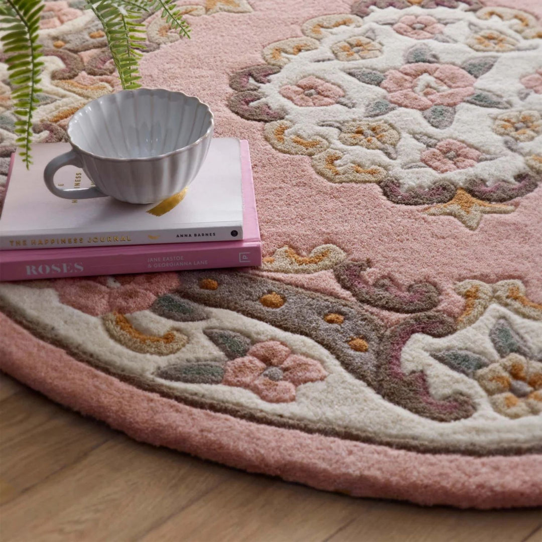 Decorative round rug with floral patterns on a wooden floor, featuring a cup and books.