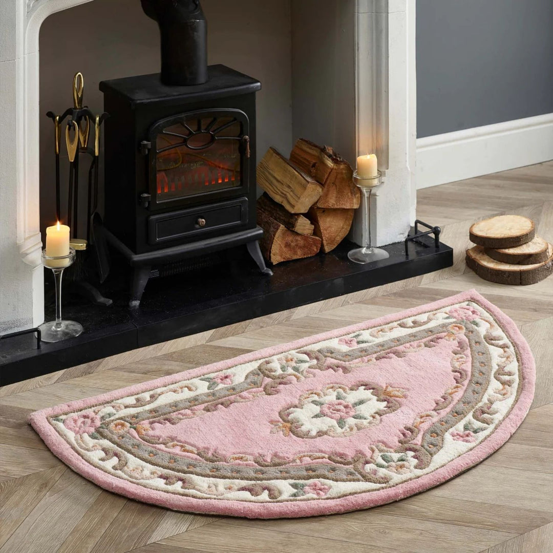Decorative pink rug on a wooden floor with a fireplace and candles in the background.