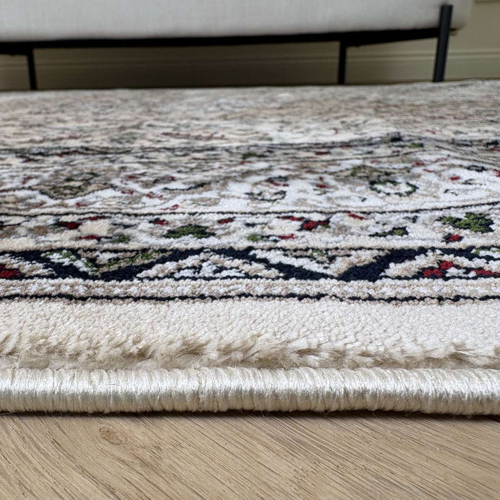 Close-up of a patterned rug on a wooden floor with a white couch in the background.