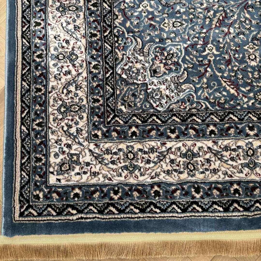 Close-up of a blue and beige patterned rug corner on a wooden floor.