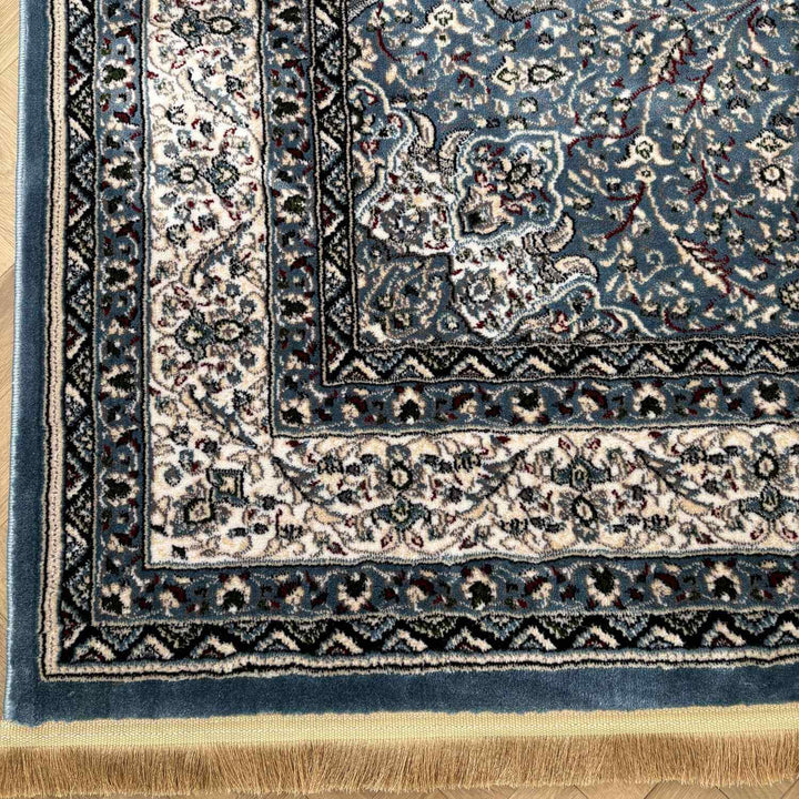 Close-up of a blue and beige patterned rug corner on a wooden floor.