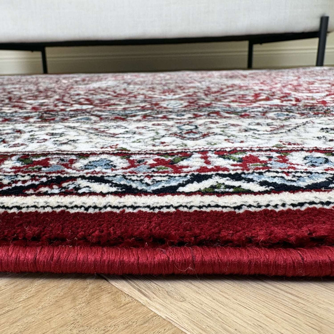 Close-up of a patterned red and white rug on a wooden floor.