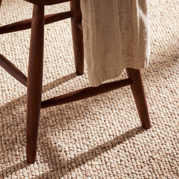 Wooden chair with a beige sweater draped over it on a textured beige carpet