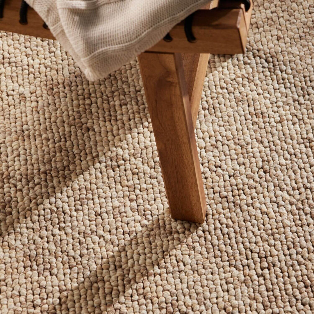 Close-up of a wooden chair leg on a textured beige carpet