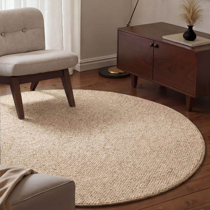Round beige rug in a living room with a chair and wooden cabinet.