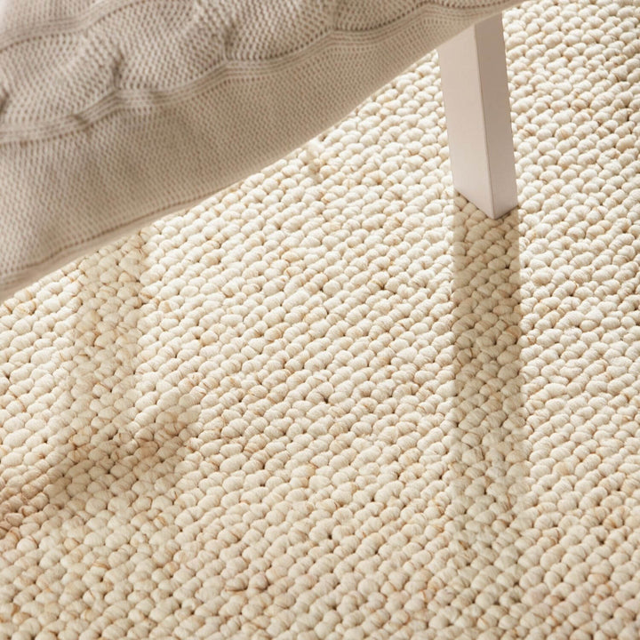Close-up of a textured beige carpet with a corner of a bed visible.