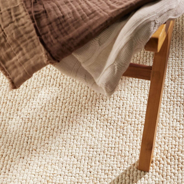 Brown and beige textured blankets draped over a wooden chair on a textured beige carpet.