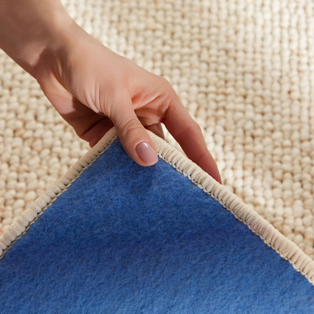 Hand pulling a blue rug away from a beige carpet