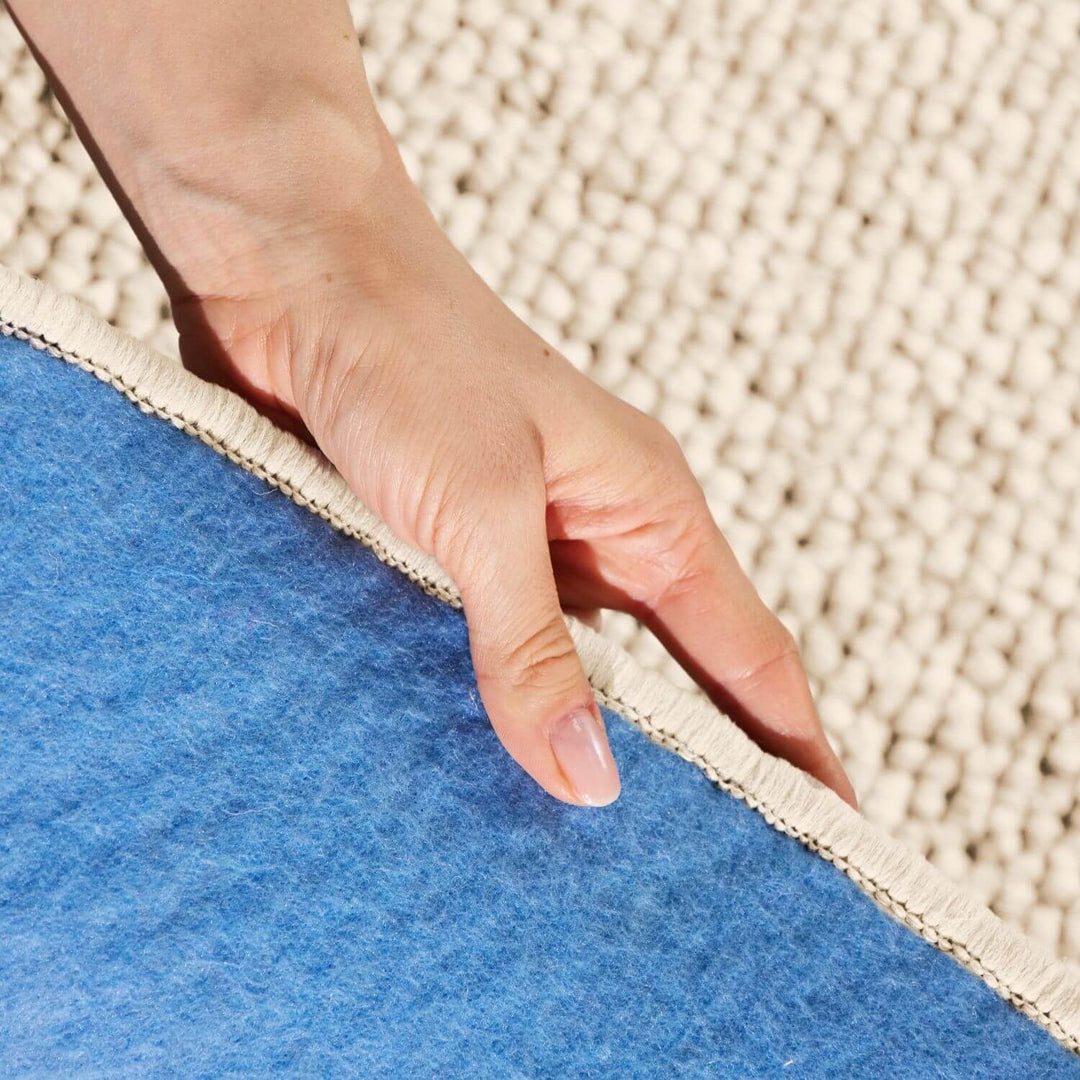 Hand touching the edge of a blue rug on a beige carpet
