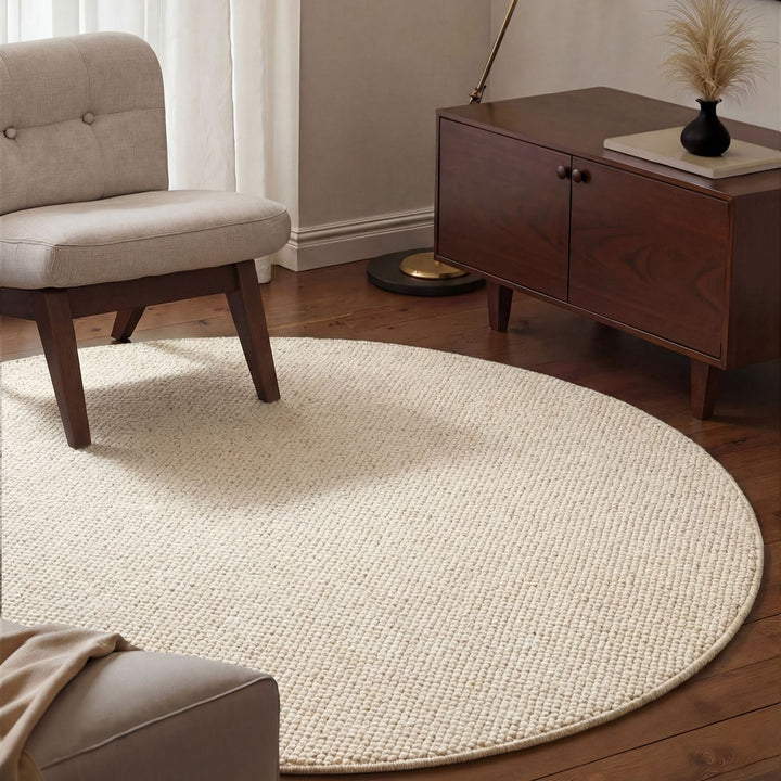 Round beige rug in a living room with a chair and wooden cabinet.