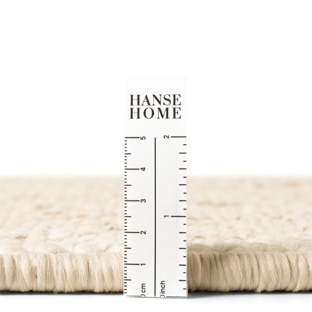 Close-up of a rug with a ruler displaying measurements and 'HANSE HOME' branding.