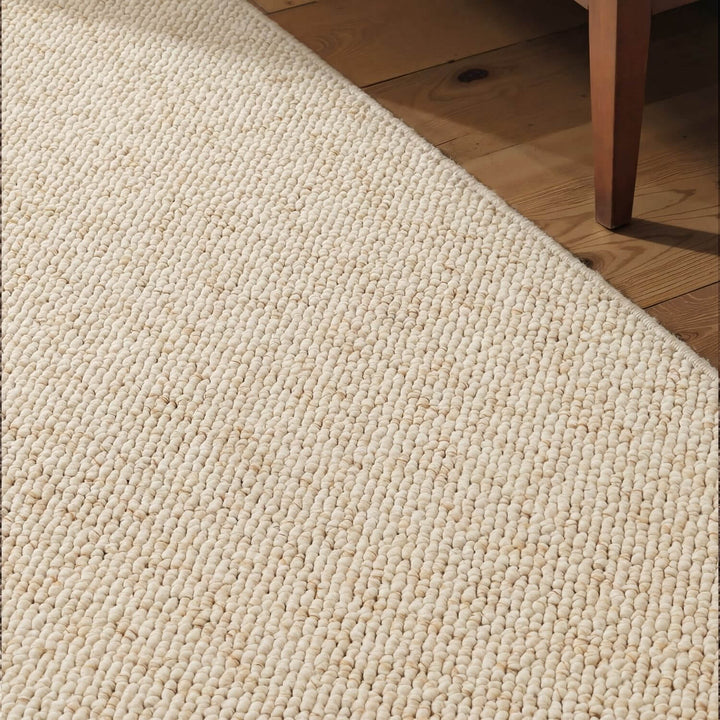 Close-up of a textured beige rug on a wooden floor.