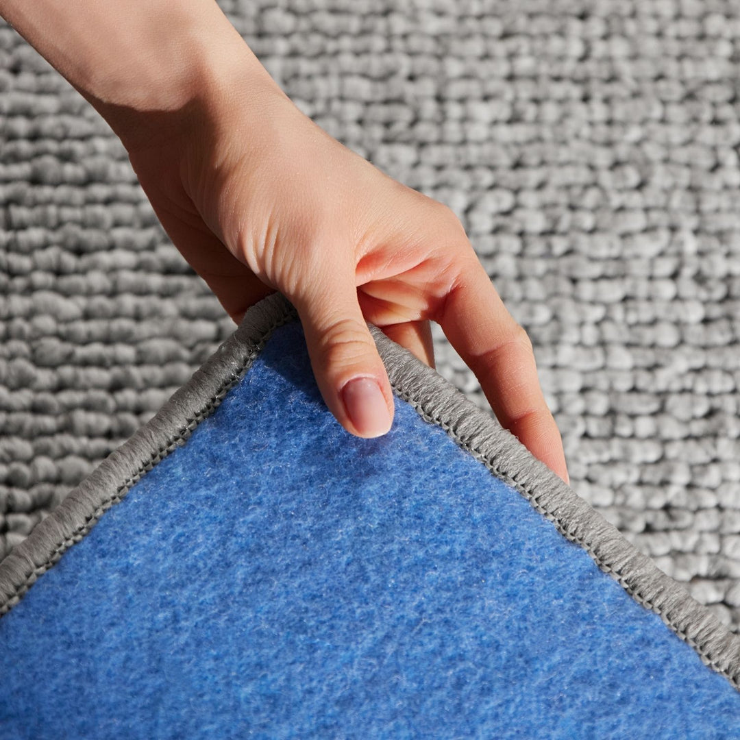 Hand lifting a blue rug from a gray carpet