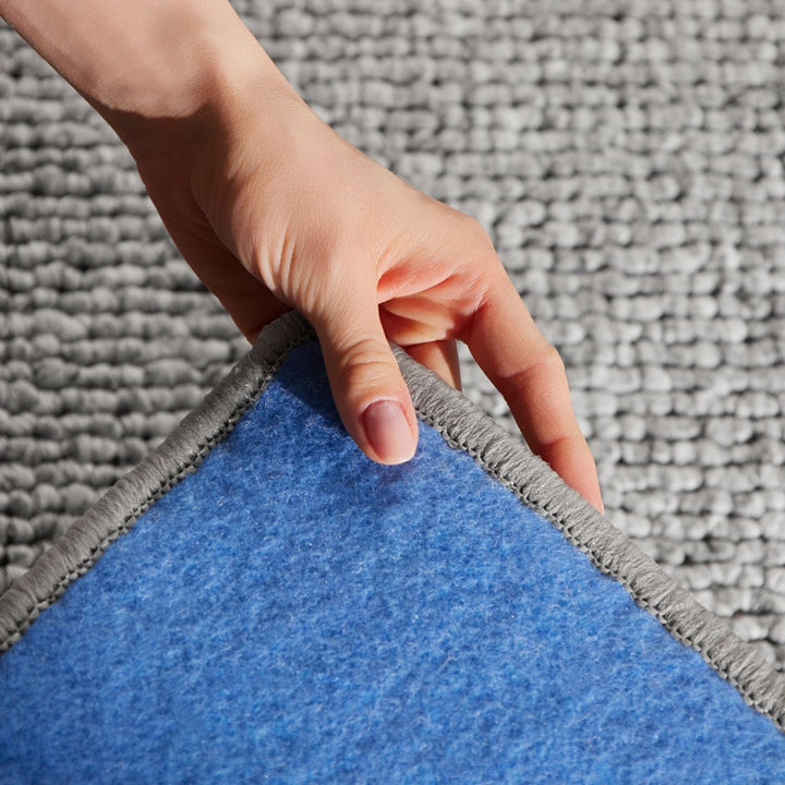 Hand lifting a blue rug from a gray carpet