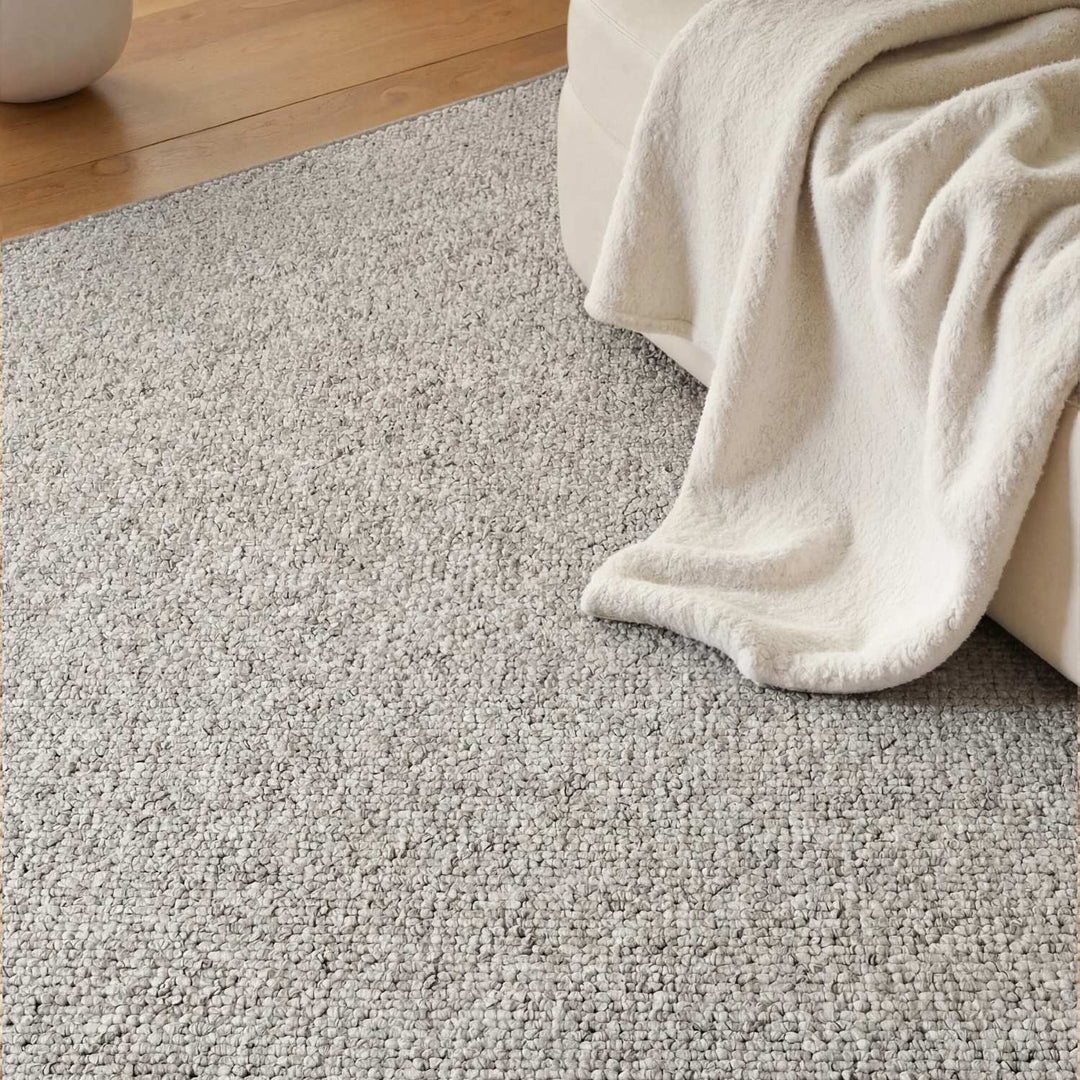 Close-up of a textured gray carpet with a beige blanket