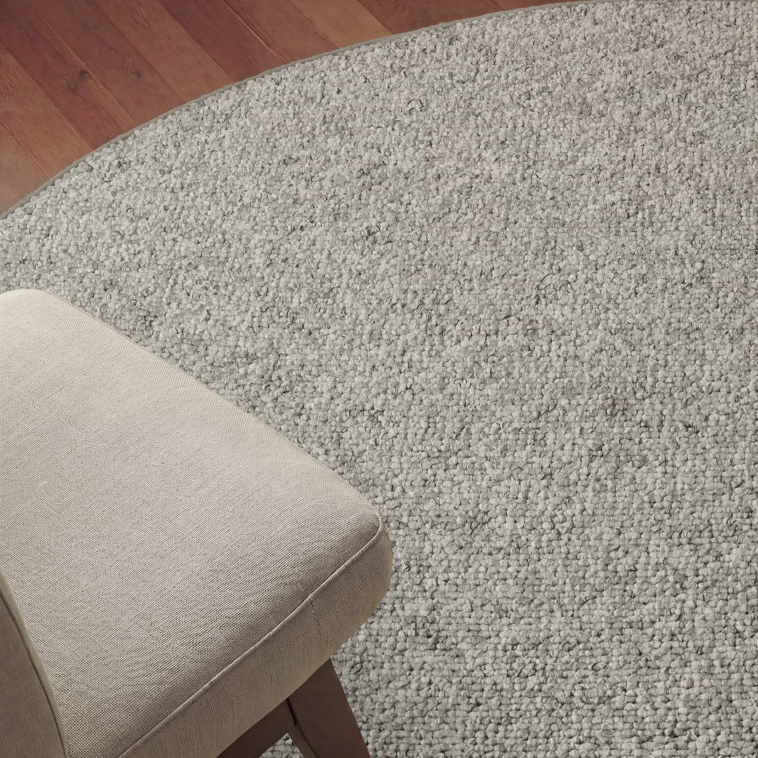 Gray textured rug on a wooden floor with a beige chair corner.