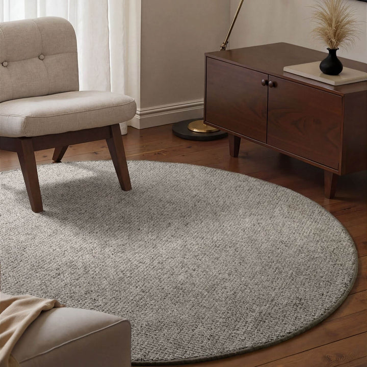 Round gray rug in a living room with a beige armchair and wooden cabinet.