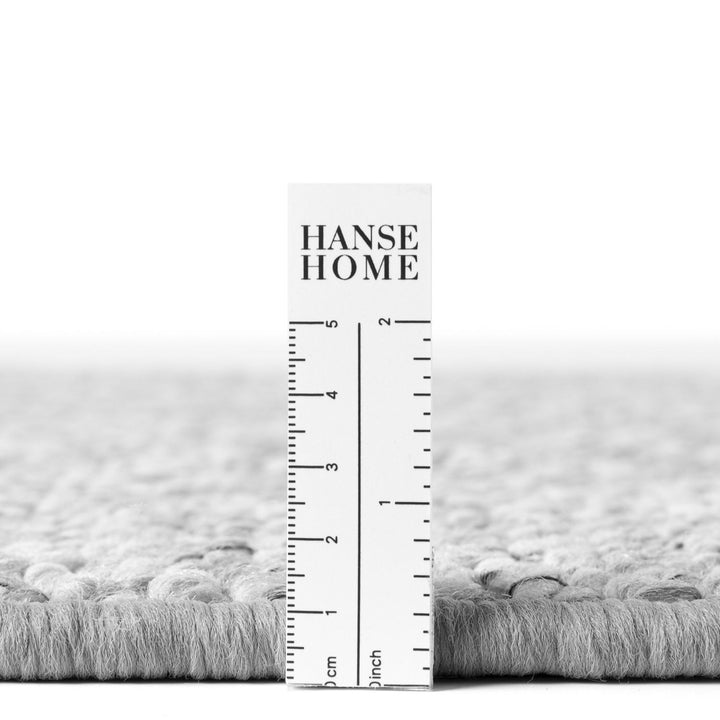 Gray textured rug with a ruler for scale and 'HANSE HOME' branding.