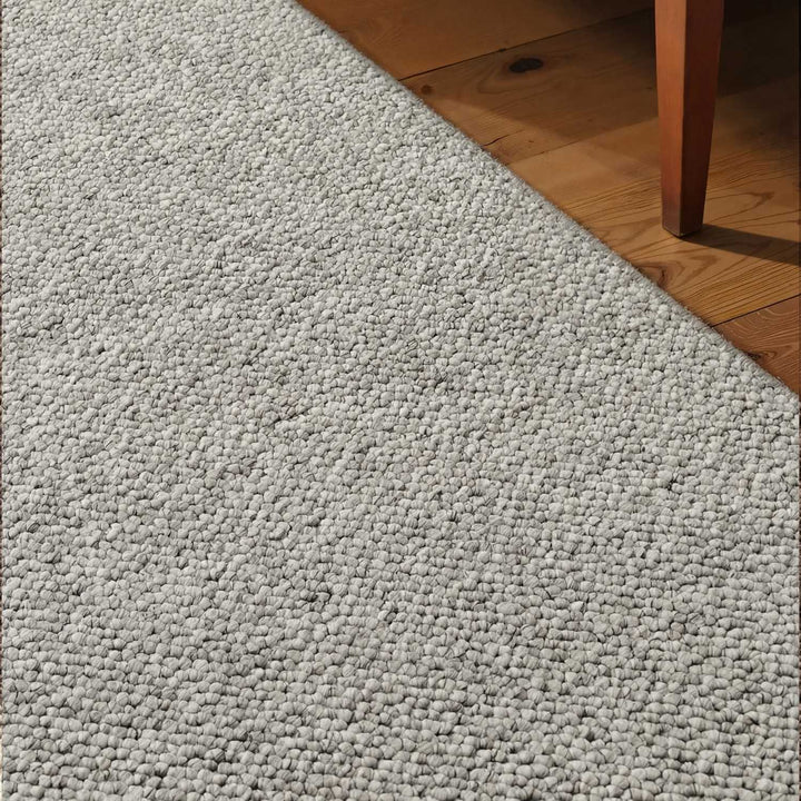 Close-up of a textured gray carpet meeting a wooden floor.