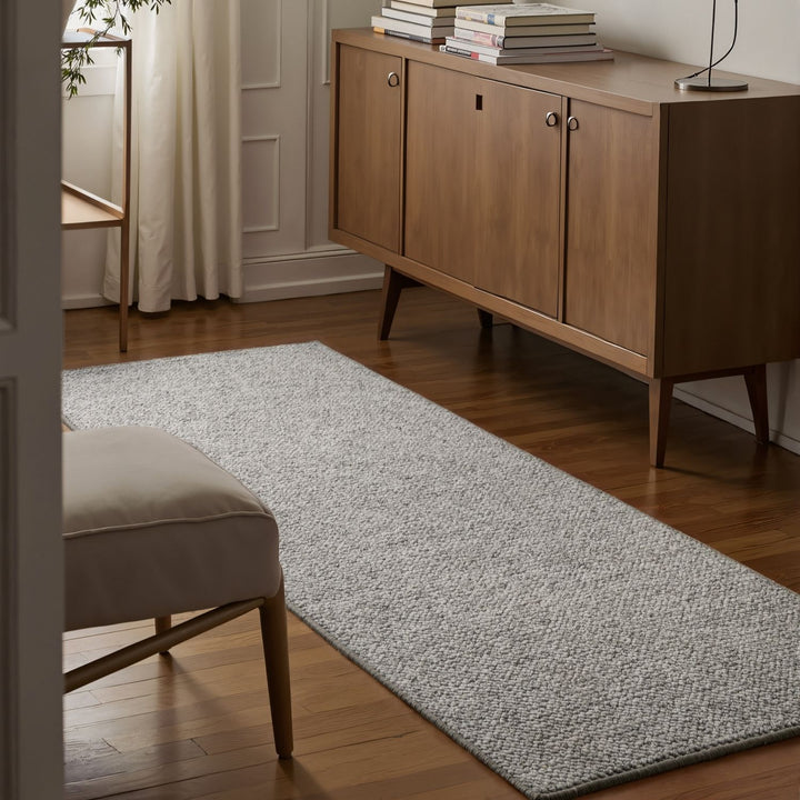 Living room with a wooden sideboard, gray rug, and beige ottoman.